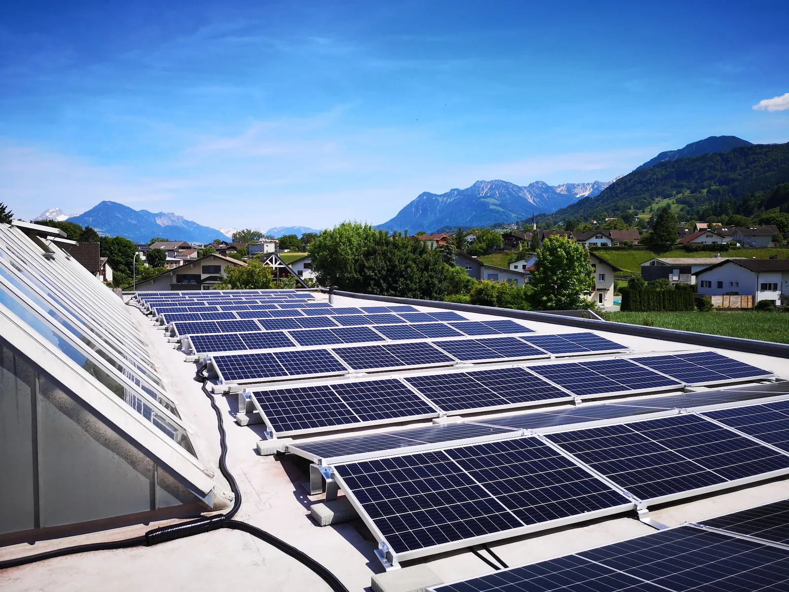 Photovoltaikmodule auf dem Flachdach des Autohauses, dahinter Häuser von Frastanz und das Bergpanorama